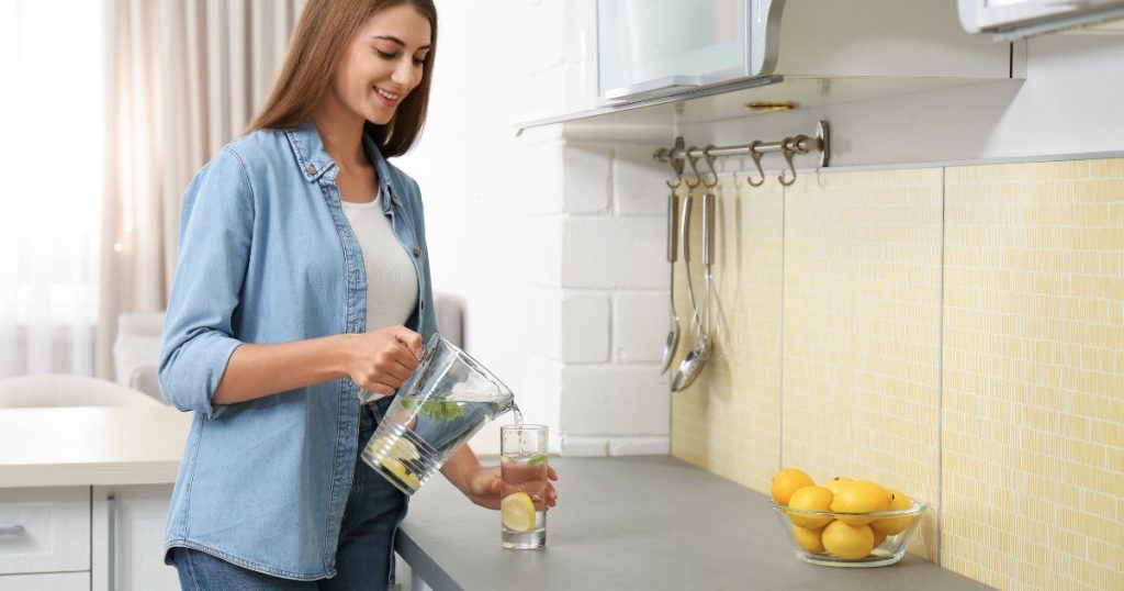 A person pouring fresh lemon juice into warm water, highlighting the simple preparation of this hydrating drink.