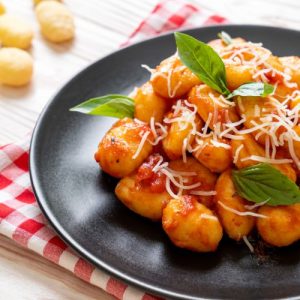 Serving of all-day gnocchi delight, forkful of gnocchi, bowl of homemade tomato sauce, sprig of fresh basil